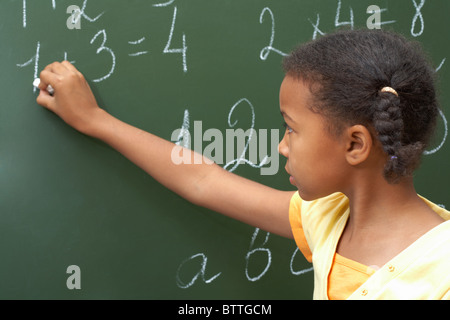 Portrait of smart schoolchild standing at blackboard and doing sums Stock Photo