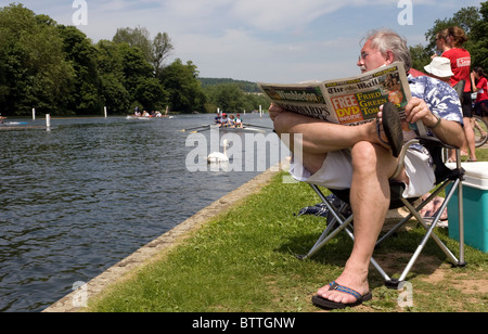A seated middle aged man reading a newspaper by the River Thames at Henley Royal Regatta Stock Photo