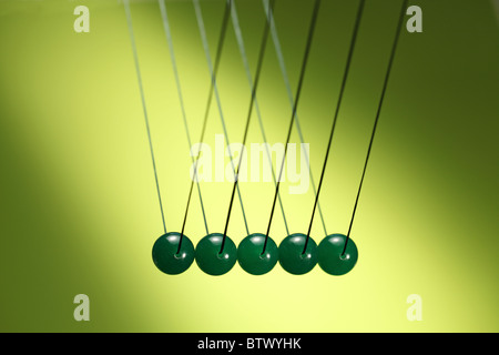 Five green marbles in row hanging from string. Illustrates Newton's cradle, a device that demonstrates conservation of momentum. Stock Photo