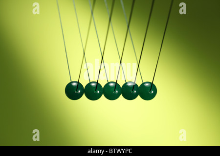 Five green marbles in row hanging from string. Illustrates Newton's cradle, a device that demonstrates conservation of momentum. Stock Photo