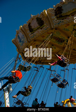 Traditional chair swing carousel in action against clear blue sky Stock Photo