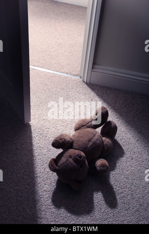 Man's legs and feett stepping past a child's teddy bear on the floor to leave the room. Stock Photo