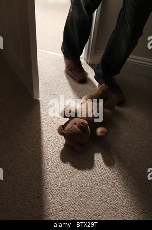Man's legs and feett stepping past a child's teddy bear on the floor to leave the room. Stock Photo