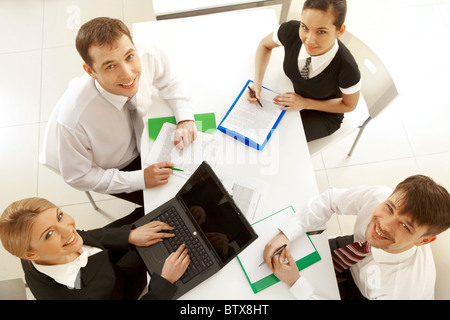 Several white collar workers looking upwards at camera from their workplaces Stock Photo