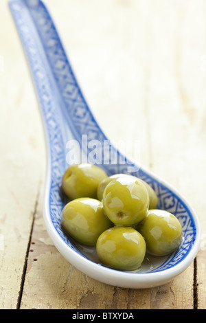 the green olives in ceramic spoon on old table Stock Photo