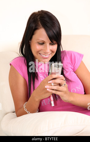 Young happy woman sitting alone on a sofa reading a message on her phone Stock Photo