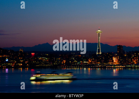 A beautiful sunrise illuminates the Space Needle and a ferry boat brings commuters into downtown Seattle, Washington.