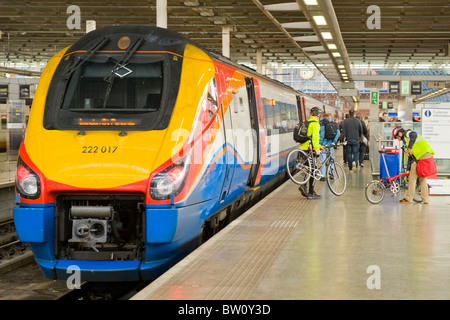 St Pancras Station , cyclists passengers disembark East Midlands engine train carriages platform clock sign customer information Stock Photo