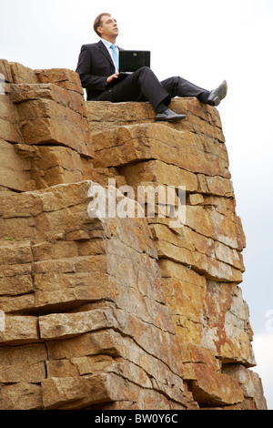 Thinking businessman with laptop sits on the top of mountain Stock Photo