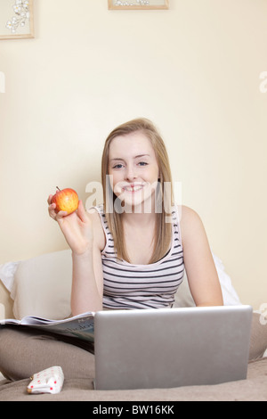 A teenage girl eats an apple whilst studying in her bedroom UK Stock Photo