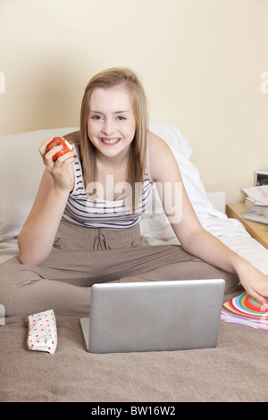 A teenage girl eats an apple whilst studying in her bedroom UK Stock Photo