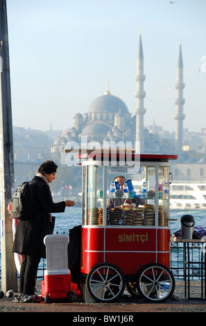 ISTANBUL, TURKEY. A customer buying a simit from one of the city's ubiquitous simit vendors, with the Yeni Mosque behind. 2010. Stock Photo