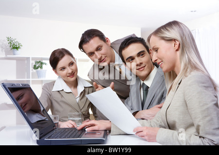 Four young businesswomen sitting at table with a laptop and examining a document Stock Photo