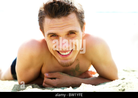 Photo of smiling guy lying on beach and looking at camera while sunbathing Stock Photo