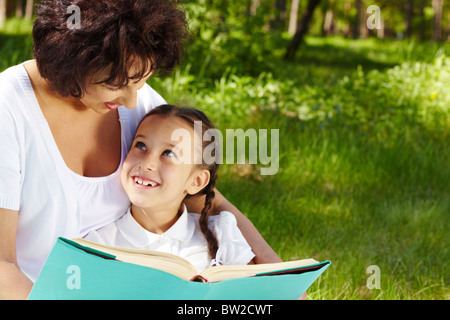 Portrait of curious girl looking at her mother while discussing book in park Stock Photo