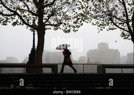 A rainy day in London, Britain. A woman rushes along under her umbrella during heavy rain storm along the embankment, central L Stock Photo