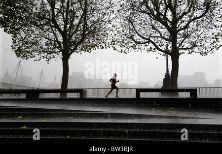 A rainy day in London, Britain. A man jogs during heavy rain storm along the embankment, central London. Stock Photo