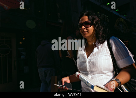 Woman in sunglasses walking on sidewalk while holding smart phone Stock Photo