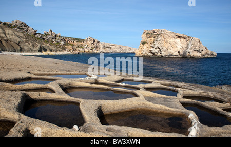 Salt pans cut in the limestone shelf at Il-Gebla Tal-Halfa, a scenic bay with an offshore isle in Qala point in Gozo in Malta.