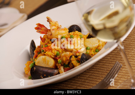 Seafood risitto dish, wine and place setting on brown woven table Stock Photo