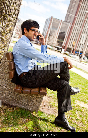 Businessman sitting on bench out side, talking on cell phone Stock Photo