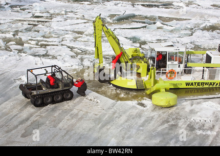 Workers on ice covered Red River during flood wearing survival suits with Amphibex ice breaker machine, Lockport, Manitoba Stock Photo