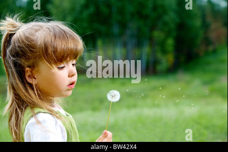 Profile of cute girl with white dandelion looking at it in the park Stock Photo