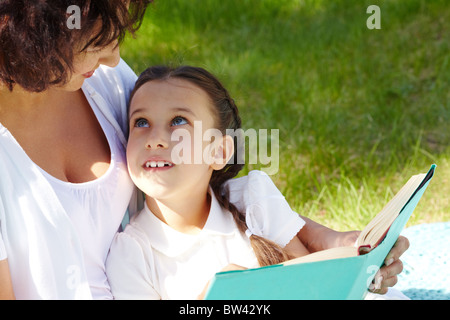Portrait of curious girl looking at her mother while discussing book in park Stock Photo
