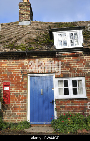 Old cottage with blue wooden front door and red post box set in brick wall, Newton Valence, Hamsphire, UK Stock Photo