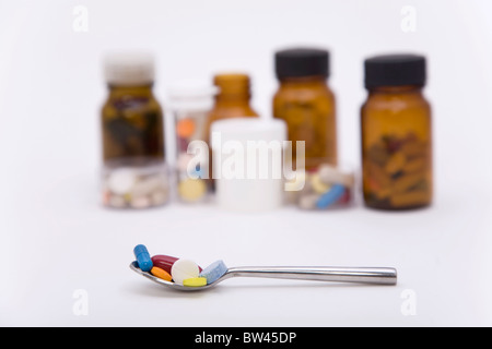 differently colored pills in spoon with other pills on the background Stock Photo