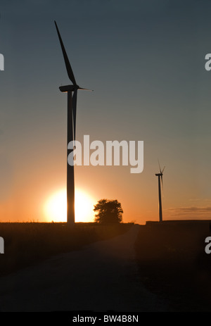 Wind turbines on an Indiana farm silhouetted behind the setting sun vertical Stock Photo