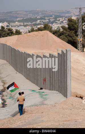 Father and daughter waving a Palestinian flag stand near the Israeli separation barrier being constructed in the West Bank. Stock Photo
