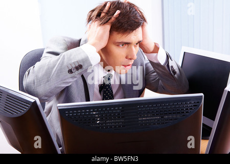 Portrait of frustrated employer surrounded by computers with his hands on head Stock Photo