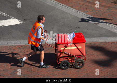 Postman hurriedly pushing his mail trolley across the road at Poole, Dorset UK in August Stock Photo