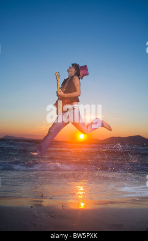 Young man jumps with guitar at sunset Stock Photo