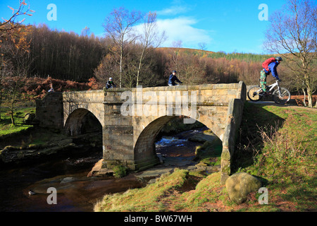 Cyclists on Slippery Stones packhorse bridge over the River Derwent, Upper Derwent Valley, Peak District National Park, Derbyshire, England, UK. Stock Photo