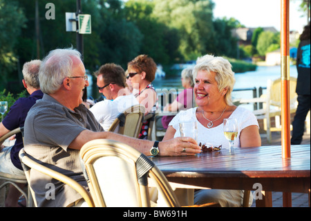 Mature white couple sitting on the edge of the Norfolk Broads enjoying a drink on a summers evening Stock Photo