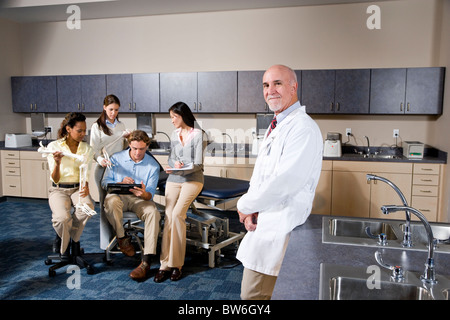 Doctor with medical trainees taking notes in background Stock Photo