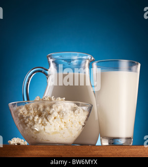Jar and glass with milk and bowl with cottage cheese on a wooden table. Stock Photo