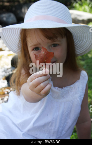 A young girl in a white hat holding a red leaf Stock Photo