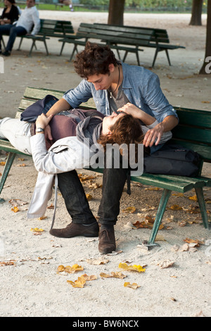 rapt young couple entwined on bench in Notre Dame Cathedral park Paris on beautiful autumn afternoon in Paris Stock Photo