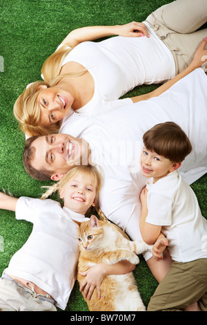 Above view of family members with pet lying on green grass and smiling at camera Stock Photo