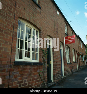 Pale yellow window-frames on brick-built Victorian terraced cottage with Estate Agents 'For Sale' sign Stock Photo