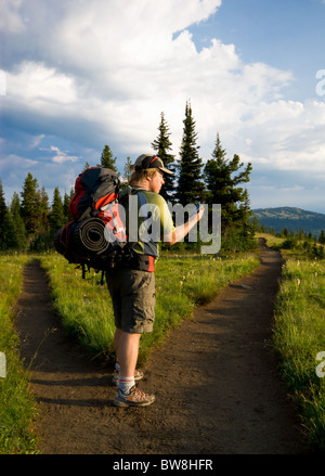 A hiker checks his GPS unit at a fork in the trail Stock Photo