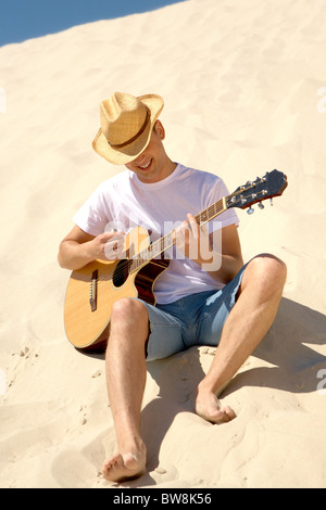 Portrait of happy man in cowboy hat playing the guitar on sandy beach Stock Photo