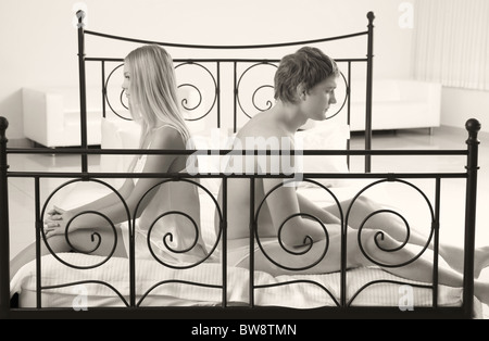 Photo of man and woman sitting on bed with sad expression Stock Photo