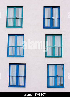 Blue patio doors and window, in a pattern on a white building wall. Taken in vertical format. Stock Photo