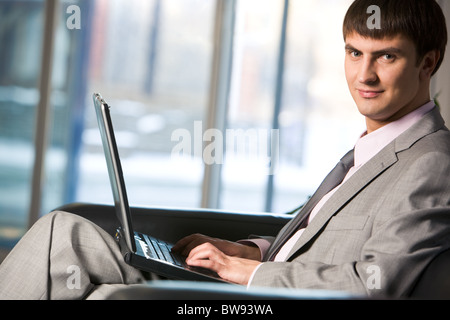 Handsome male typing on keyboard of laptop and looking at camera Stock Photo