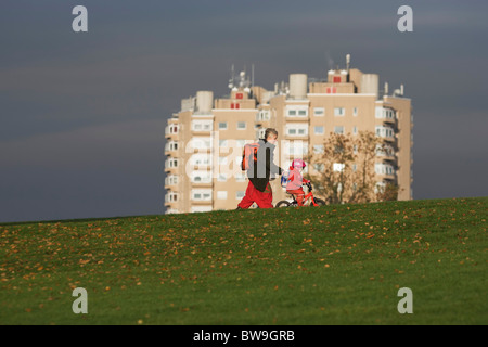 Local mother and child on bike with high-rise flats seen from Brockwell Park, Herne Hill, South London. Stock Photo