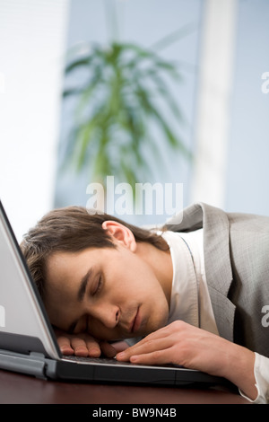 Sleeping man with his head put onto keyboard of laptop having rest in office Stock Photo